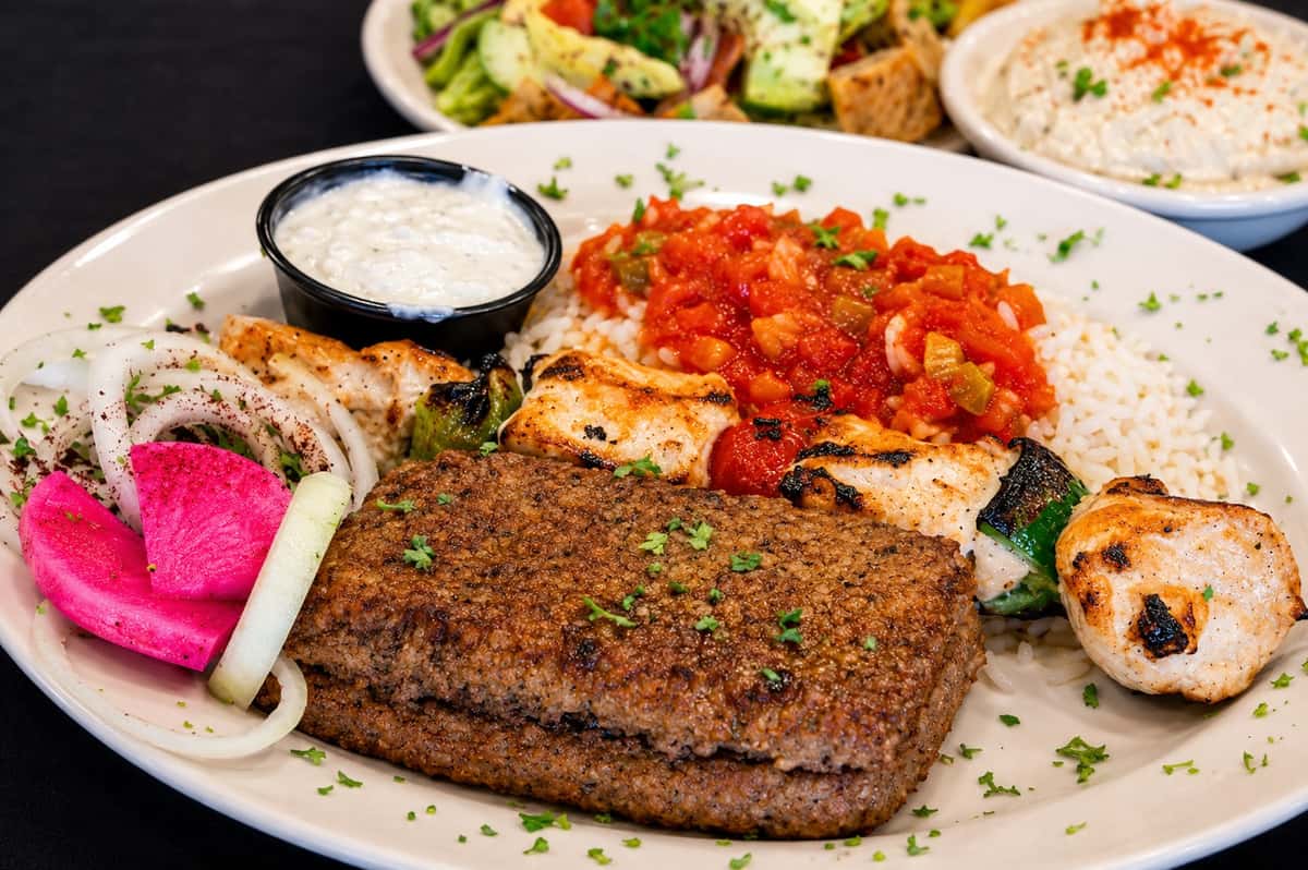 Baked kibbeh served with rice, grilled chicken, tomato sauce, onions, pickled turnips, and dipping sauces