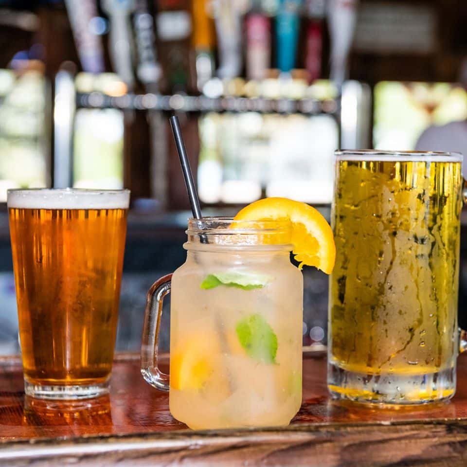 A lemon cocktail and two glasses of beer on the bar countertop