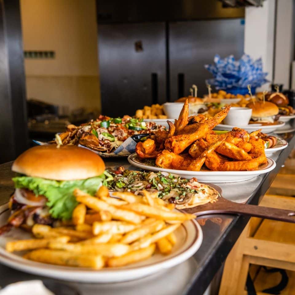 Multiple plates filled with different menu items such as fried fish, flatbread pizzas and burgers
