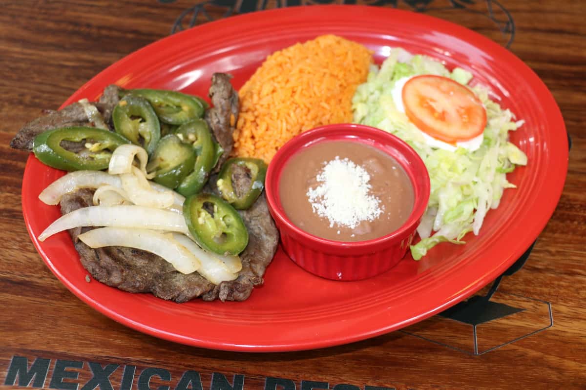Grilled pork chop topped with sautéed onions, served with Mexican rice, shredded lettuce, tomato, and refried beans.