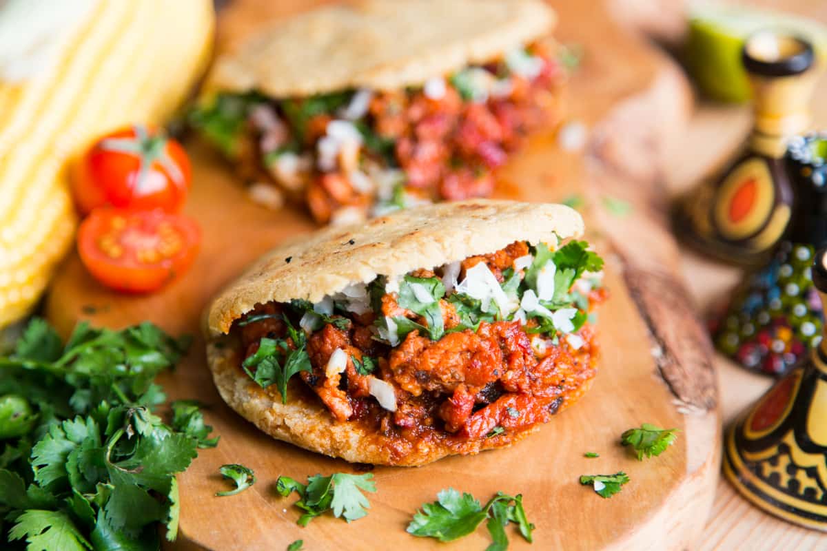 A delicious Mexican sope topped with seasoned ground meat, fresh cilantro, diced onions, and a side of vibrant cherry tomatoes and corn.