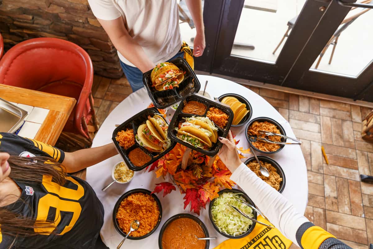 Friends sharing takeout tacos with rice, beans, and sides around a table—casual Mexican dining and group meal experience.
