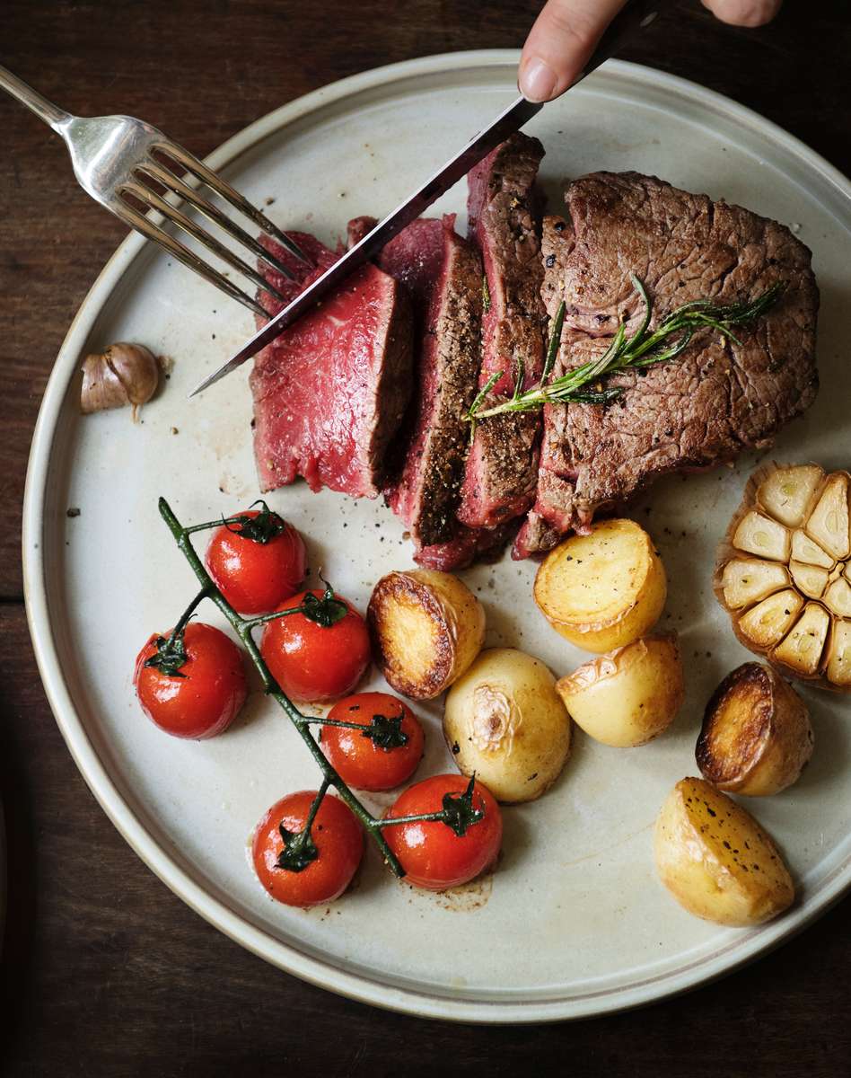 Close-up of a perfectly cooked fillet steak, sliced, served with roasted potatoes, garlic, and cherry tomatoes