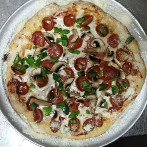 Pizza pie on silver pizza tray. Toppings include pepperoni, mushrooms, peppers.