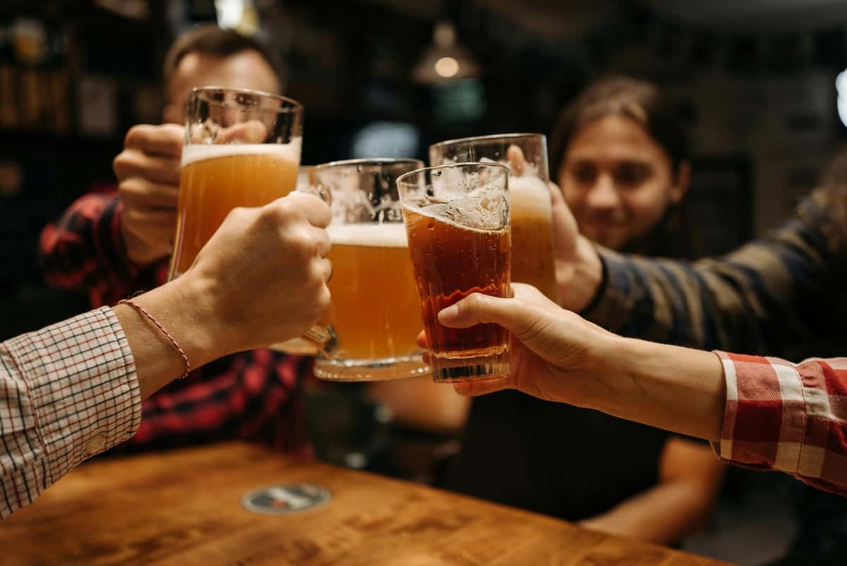 Friends toasting with pint glasses of beer at a bar, celebrating together around a wooden table.