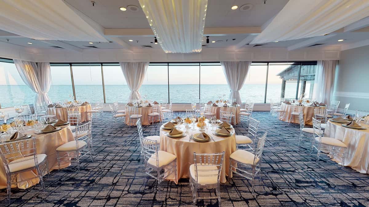 Elegant oceanfront wedding ballroom with round tables, draped ceilings, and floor-to-ceiling waterfront views