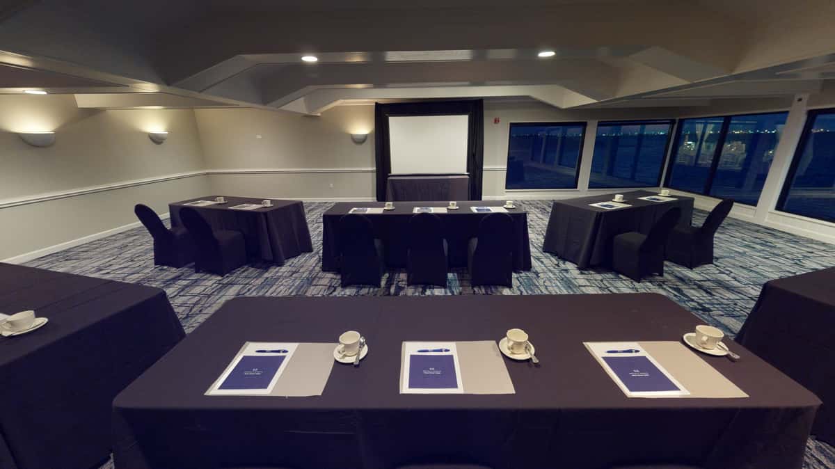 Professional waterfront meeting room with classroom-style seating, presentation screen, and conference tables for corporate events