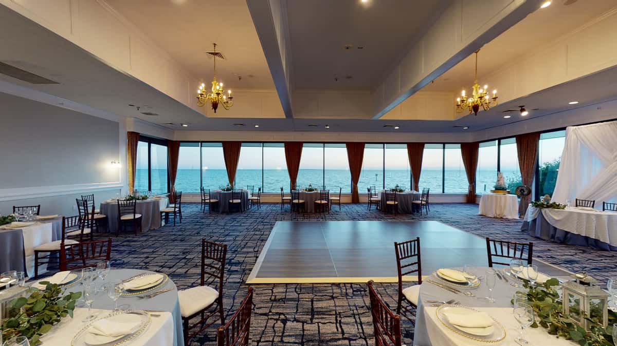 Spacious waterfront wedding reception venue with dance floor, banquet tables, and panoramic ocean views through floor-to-ceiling windows