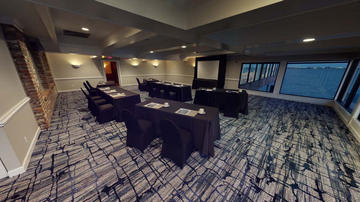 Private waterfront conference room with U-shaped meeting setup, presentation screen, and panoramic bay views for business events