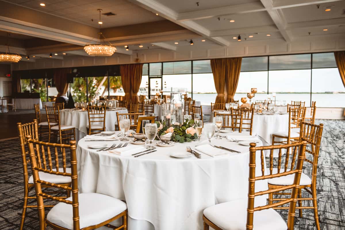Elegant waterfront wedding reception with gold chiavari chairs, candlelit tables, and panoramic sunset views