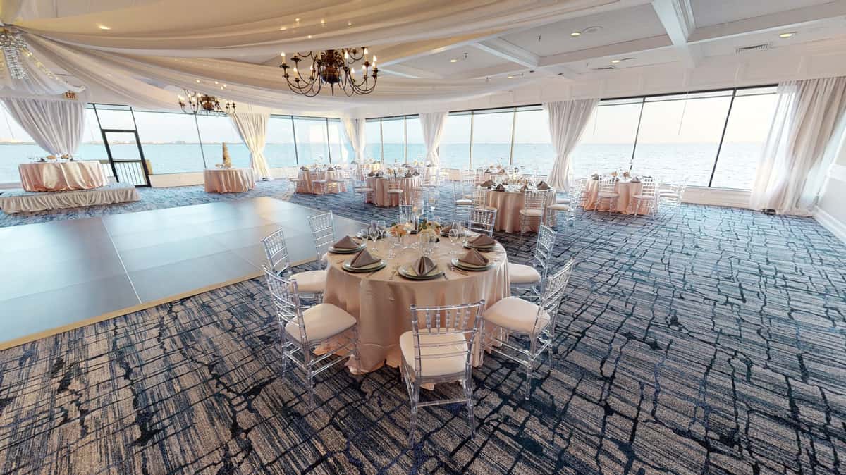 Bright oceanfront wedding ballroom with draped ceilings, dance floor, and elegant round tables overlooking the water