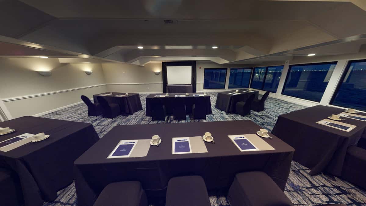 Private waterfront meeting room with classroom-style conference setup, presentation screen, and panoramic bay views