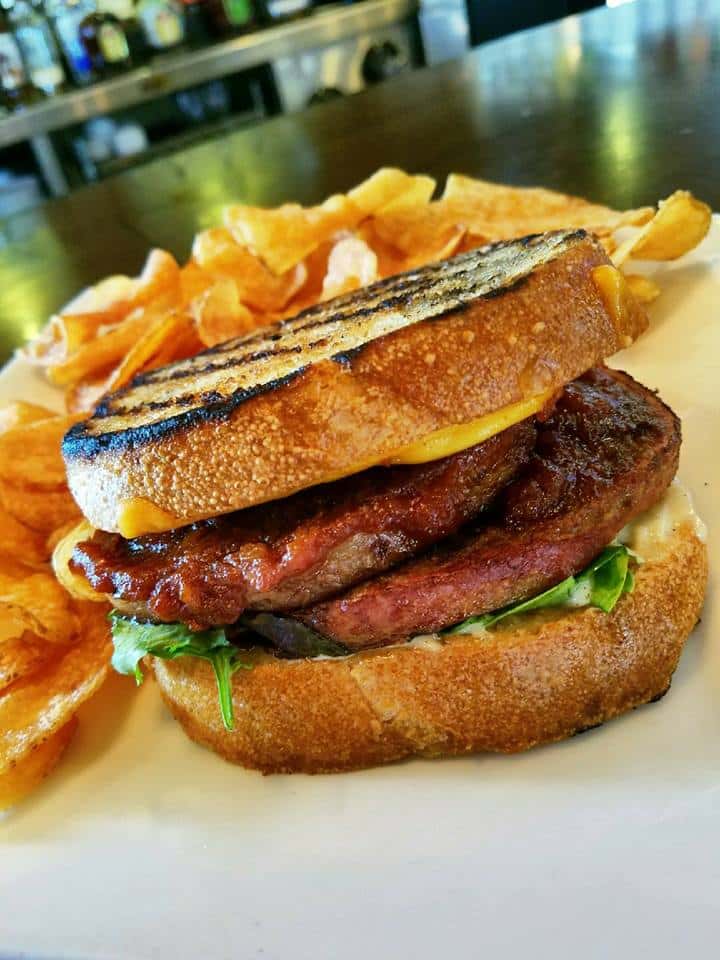 two patty burger on a roll with a side of chips