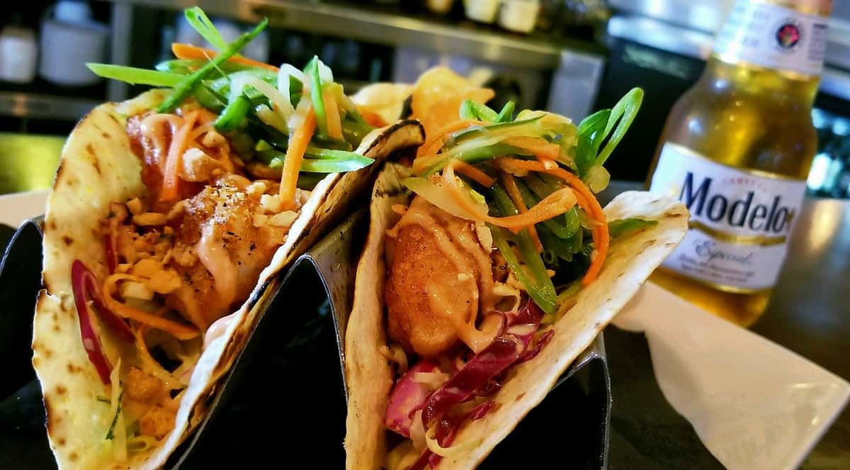 soft shell tacos in metal holders topped with sauce and coleslaw