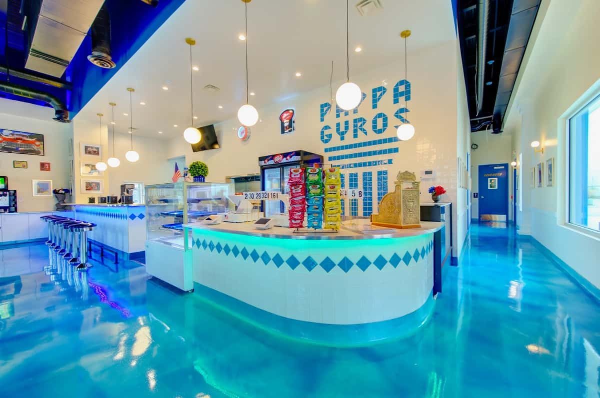 Bright and colorful interior of Pappa Gyros featuring blue floors, white walls, retro stools, and a snack-filled front counter.
