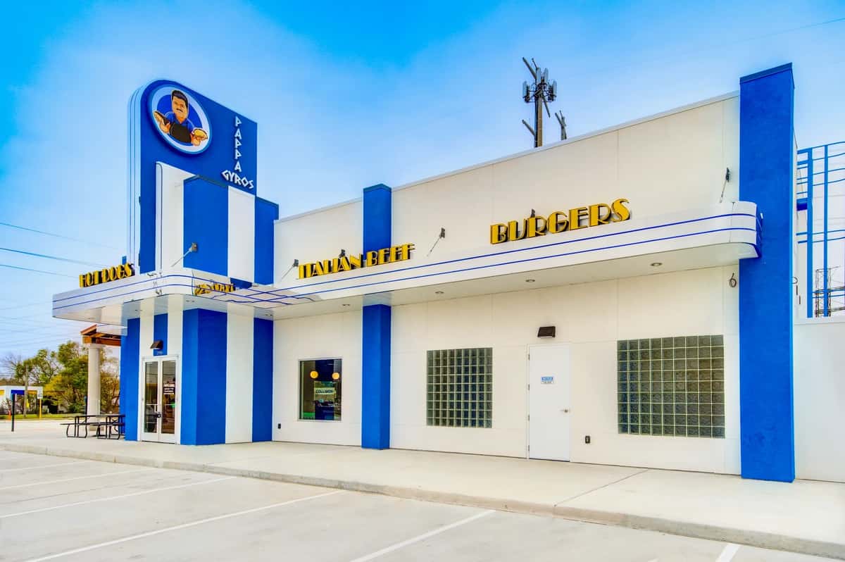 Pappa Gyros restaurant with a white and blue exterior, bold yellow signage, and a tall sign featuring the brand's cartoon mascot.