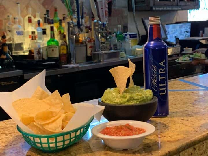 basket of tortilla chips, guacamole, salsa and bottle of beer on the bar