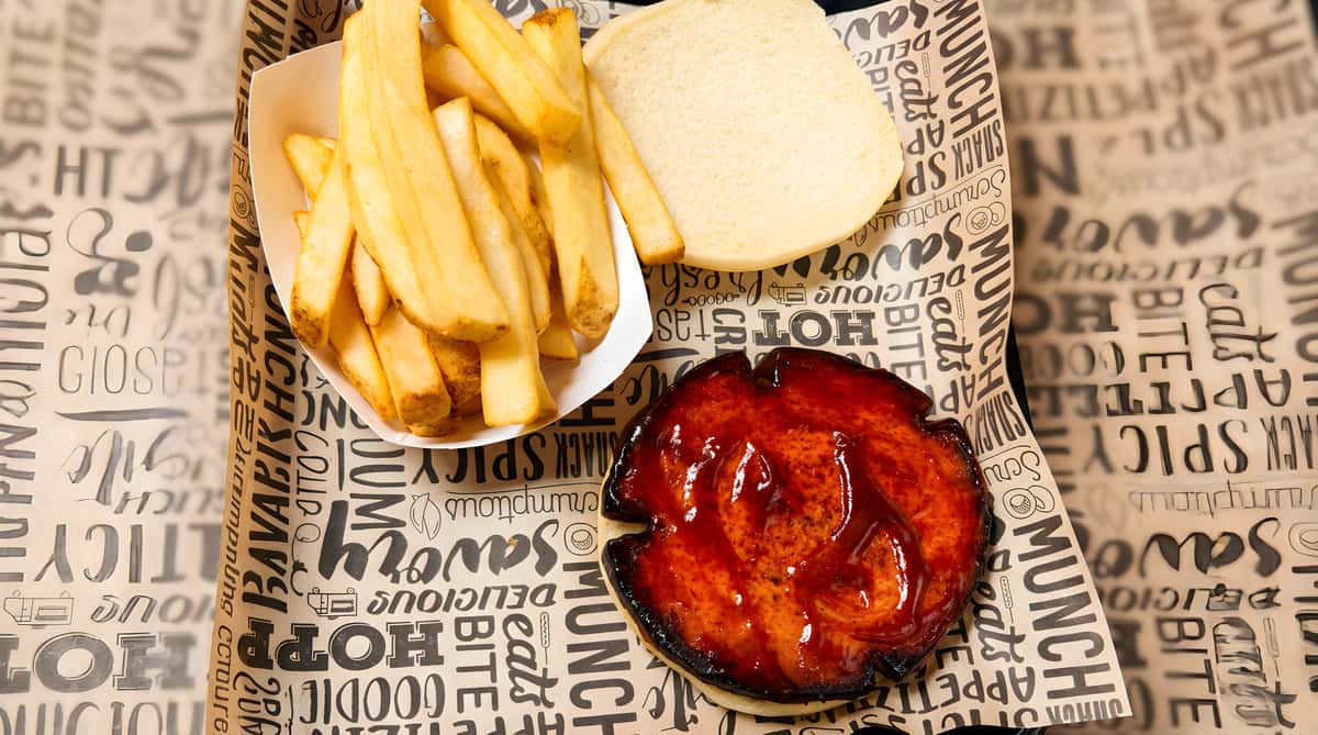 BBQ burger patty with a plain bun and a side of golden French fries served on patterned paper.