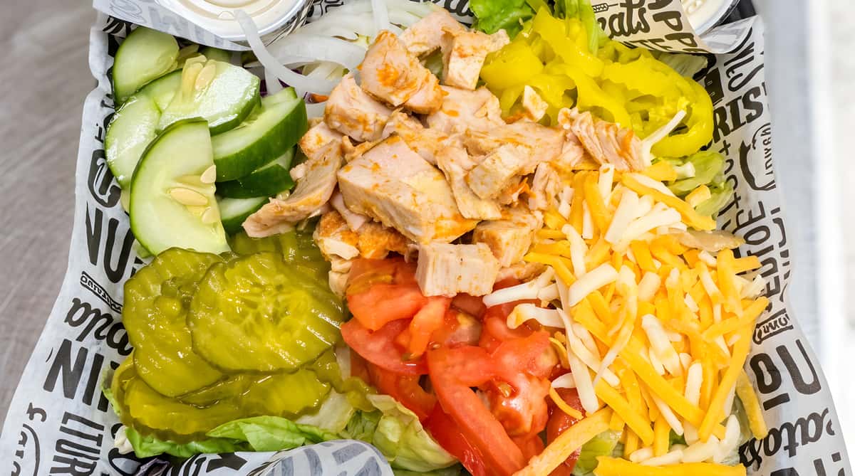 Salad with diced chicken, sliced cucumbers, pickles, tomatoes, yellow peppers, and shredded cheddar cheese on a bed of lettuce.
