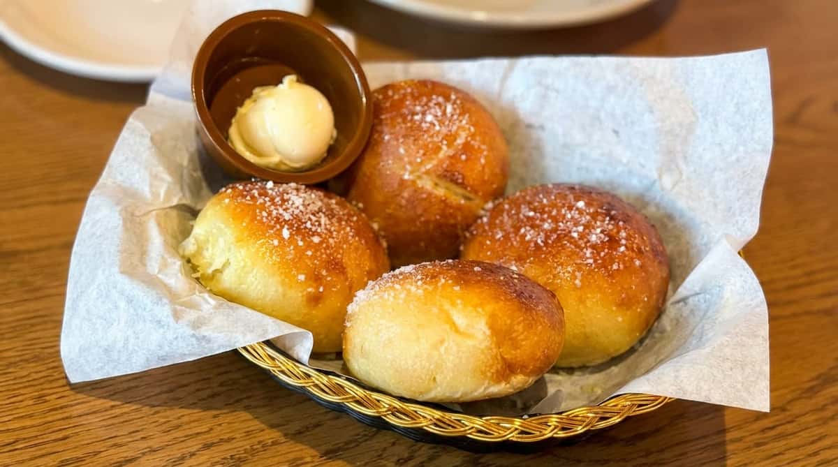 Bread rolls dusted with parmesan cheese in a wicker basket with a cup of butter.