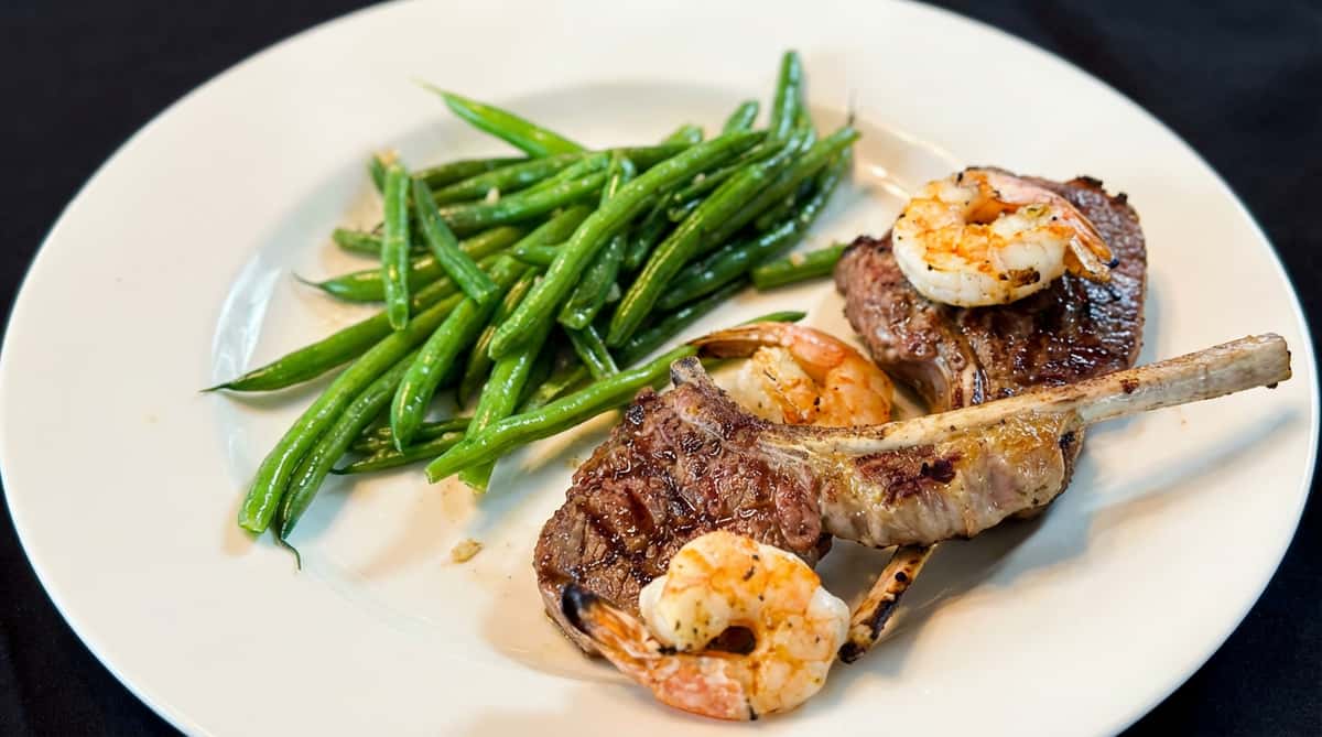 Lamb chops and shrimp with green beans on a white plate.