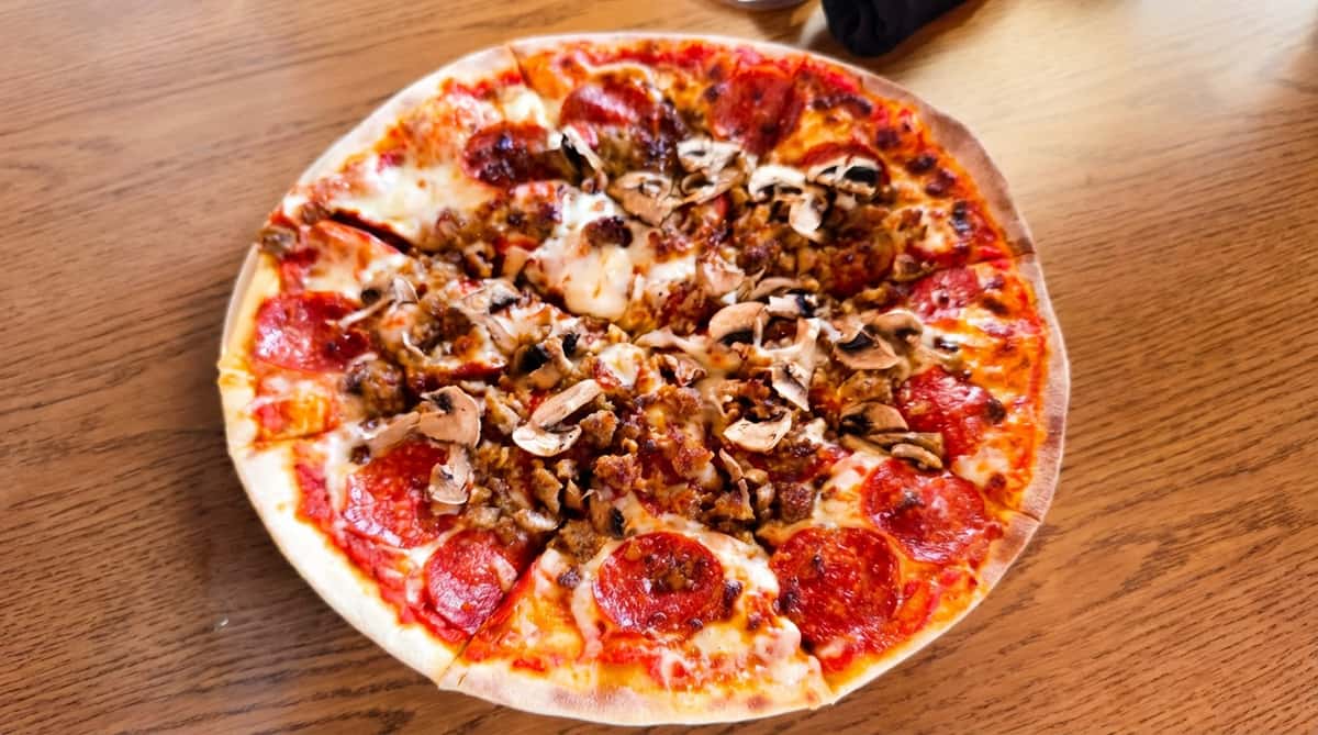 Pizza with pepperoni, sausage, and mushrooms on a wooden table.