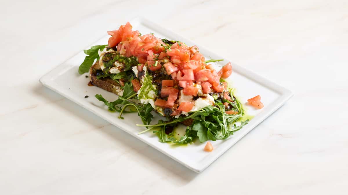 Creamy burrata and fresh avocado on toasted multigrain bread, topped with diced tomatoes, arugula and drizzled with pesto and balsamic reduction