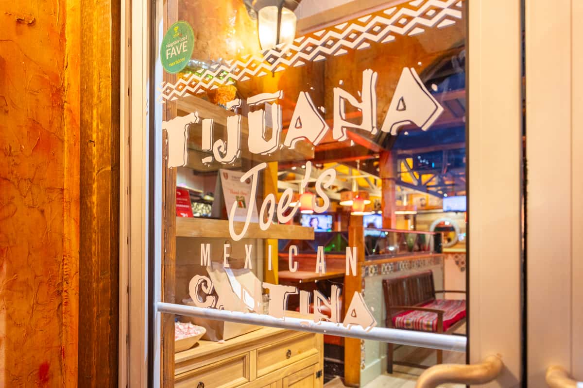 Tijuana Joe's Mexican Cantina entrance window with bold white lettering, warm ambient lighting, and a vibrant interior featuring colorful décor and booth seating, capturing the inviting atmosphere of a lively Tex-Mex restaurant.