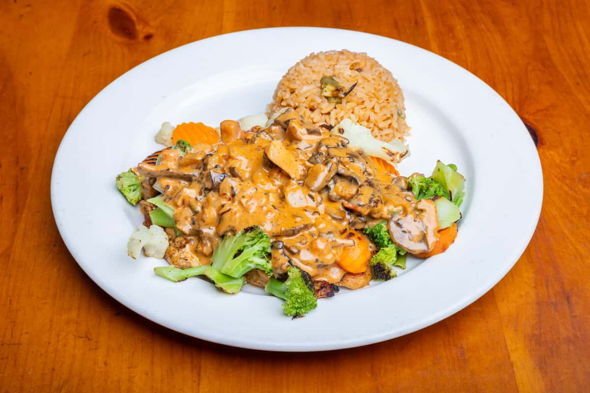 Grilled chicken topped with creamy mushroom sauce, served with Mexican rice and sautéed mixed vegetables including broccoli, carrots, and cauliflower on a white plate.