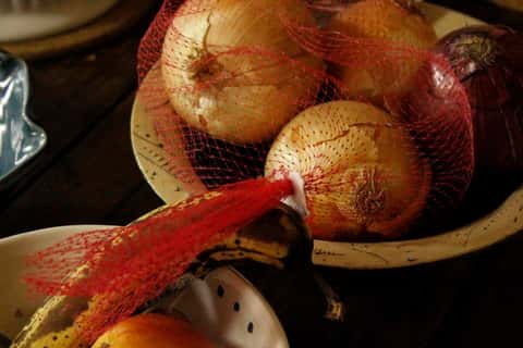 Raw onions in sack in bowl on counter