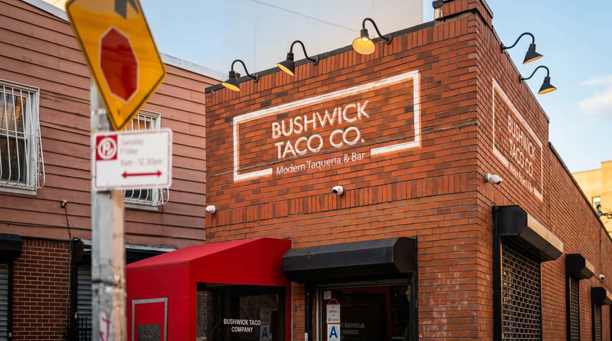 Brick building with "Bushwick Taco Co." sign, red awning, and a blurred stop sign.