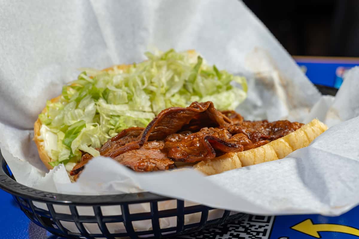 Open roast beef po'boy sandwich served in a paper-lined basket, featuring slow-cooked sliced beef smothered in rich brown gravy and topped with shredded lettuce on a toasted hoagie roll, set on a blue branded table at Darrell's restaurant.