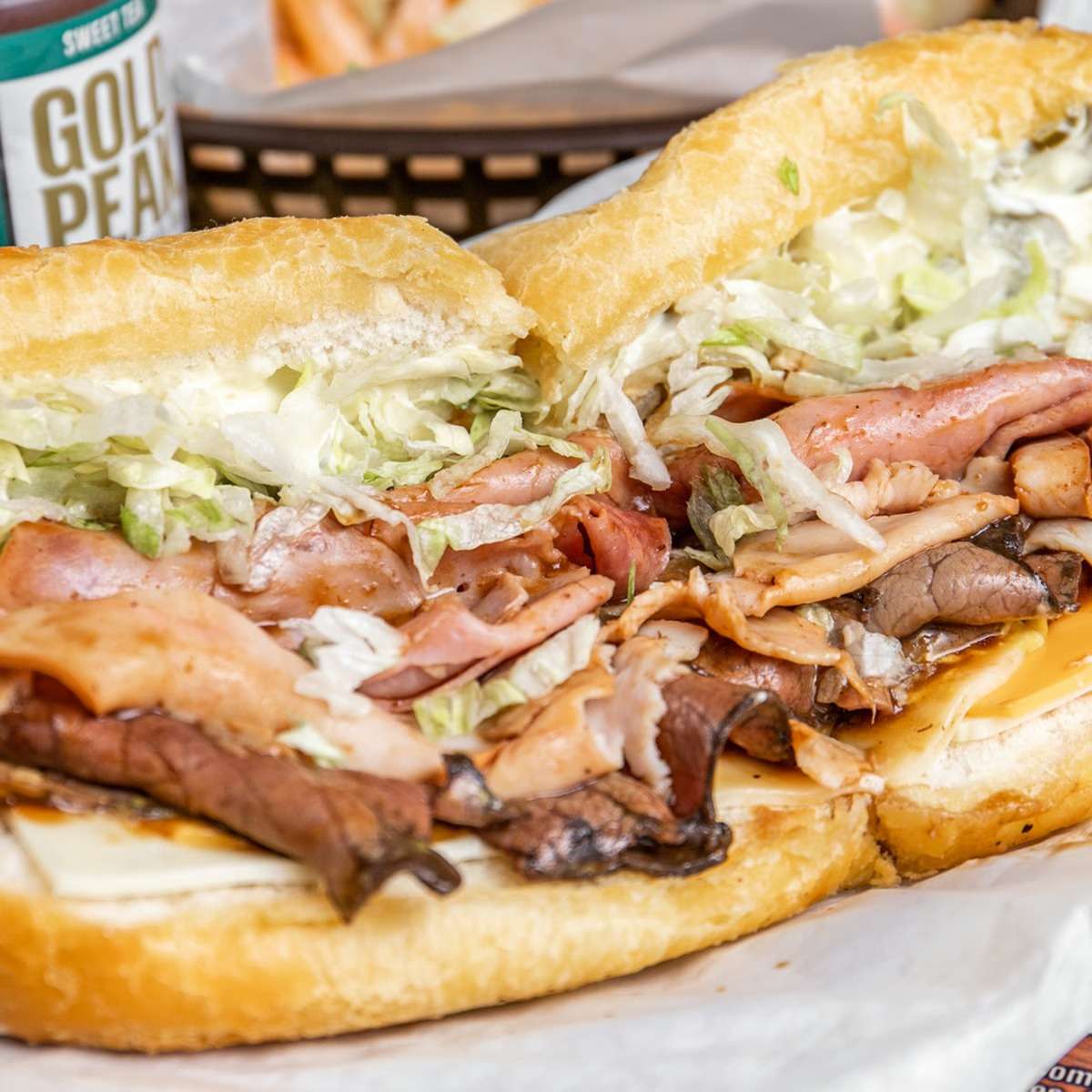 Stacked po'boy sandwich loaded with ham, turkey, roast beef, shredded lettuce, and cheese on toasted French bread, capturing the bold flavors of a Southern-style deli classic.