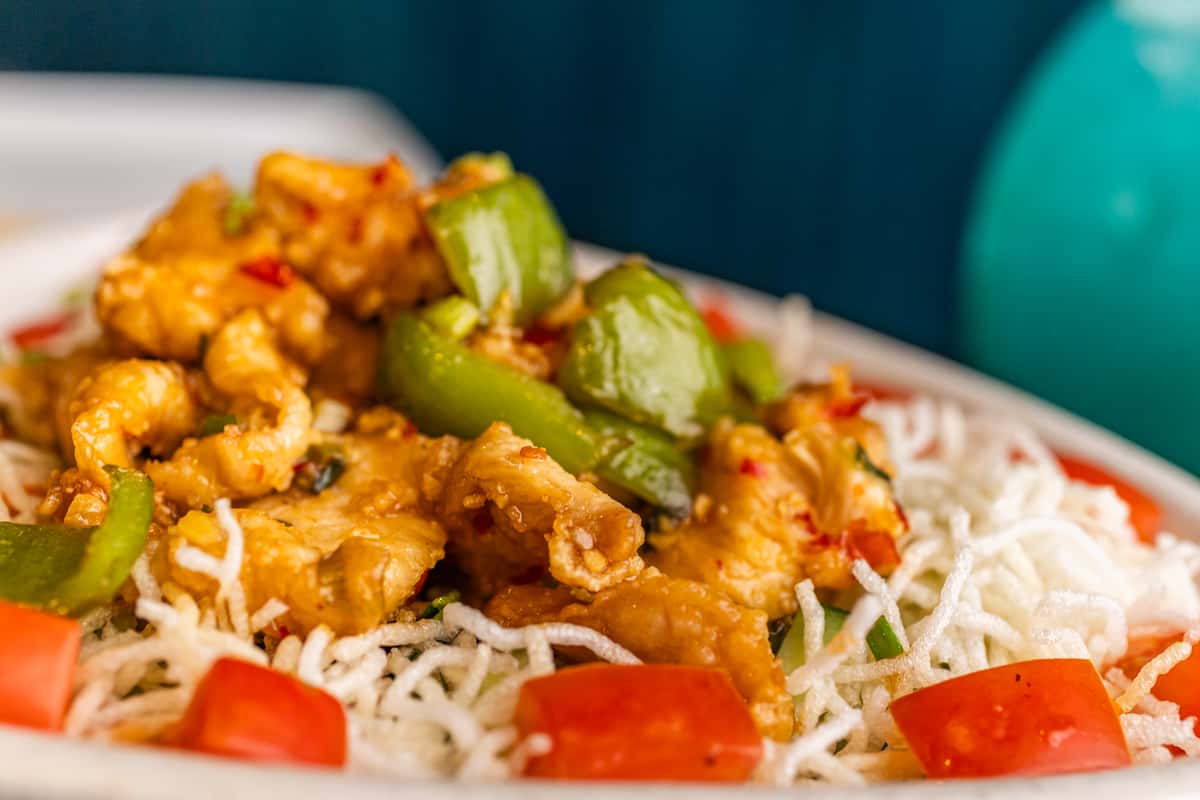 Crispy stir-fried chicken with green bell peppers, served over crunchy fried rice noodles and garnished with diced tomatoes.