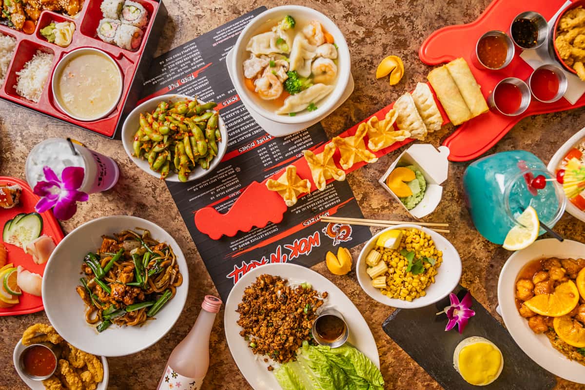 Vibrant Asian fusion feast with lo mein, dumpling soup, edamame, lettuce wraps, fried appetizers, sushi, and colorful cocktails.