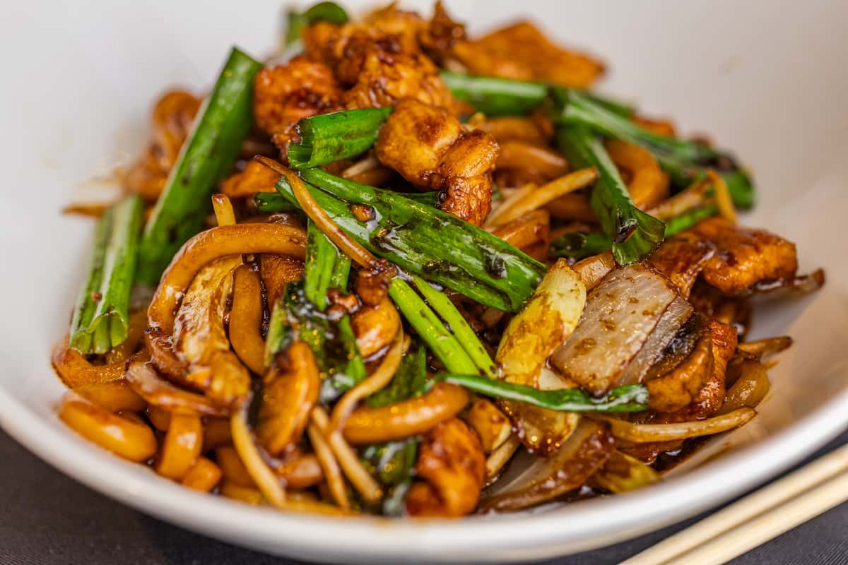 Stir-fried noodles with grilled chicken, green onions, and caramelized onions in a savory brown sauce.