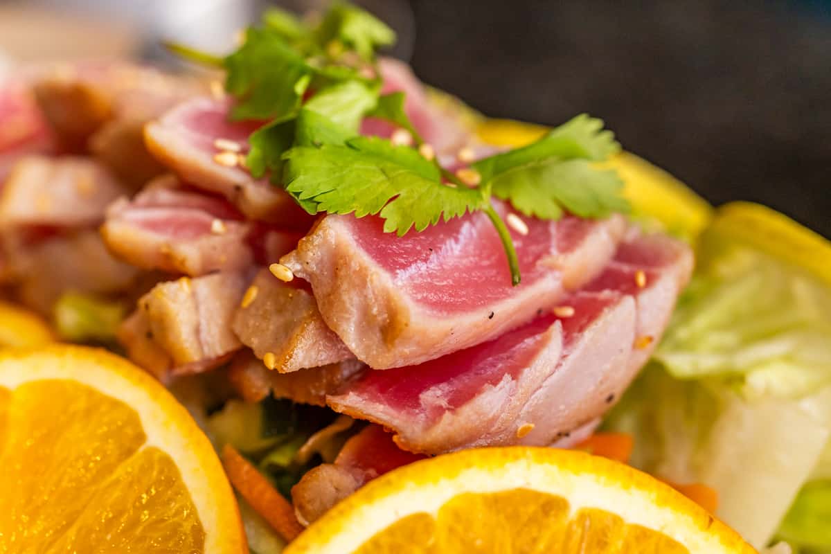 Seared ahi tuna slices topped with cilantro and sesame seeds, served on mixed greens with fresh orange slices.