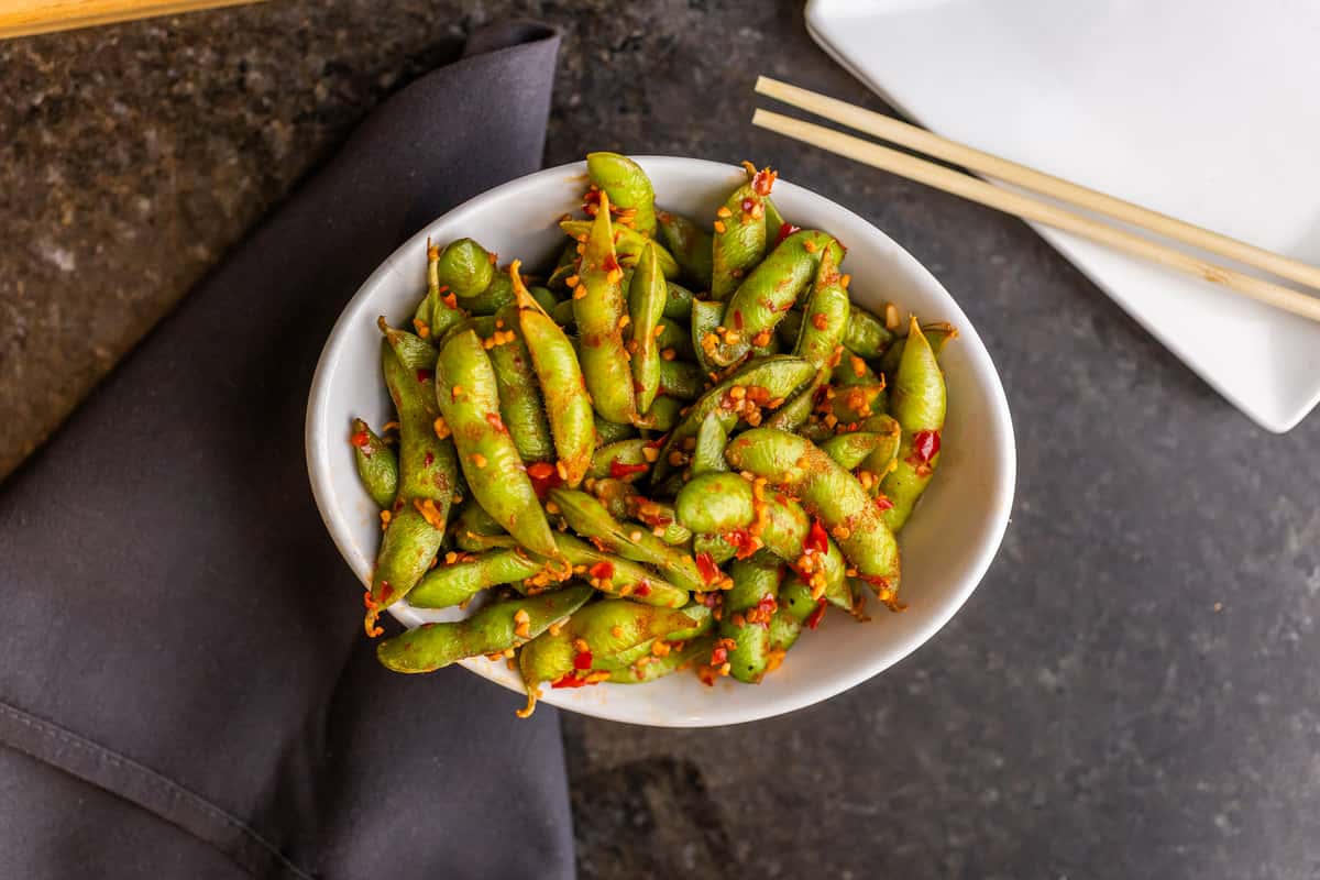 Spicy garlic edamame, stir-fried with chili flakes and minced garlic, served in a white bowl.