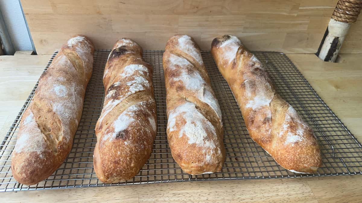 reshly baked artisan baguettes with golden, crusty exteriors and a dusting of flour, cooling on a wire rack in a rustic bakery setting.