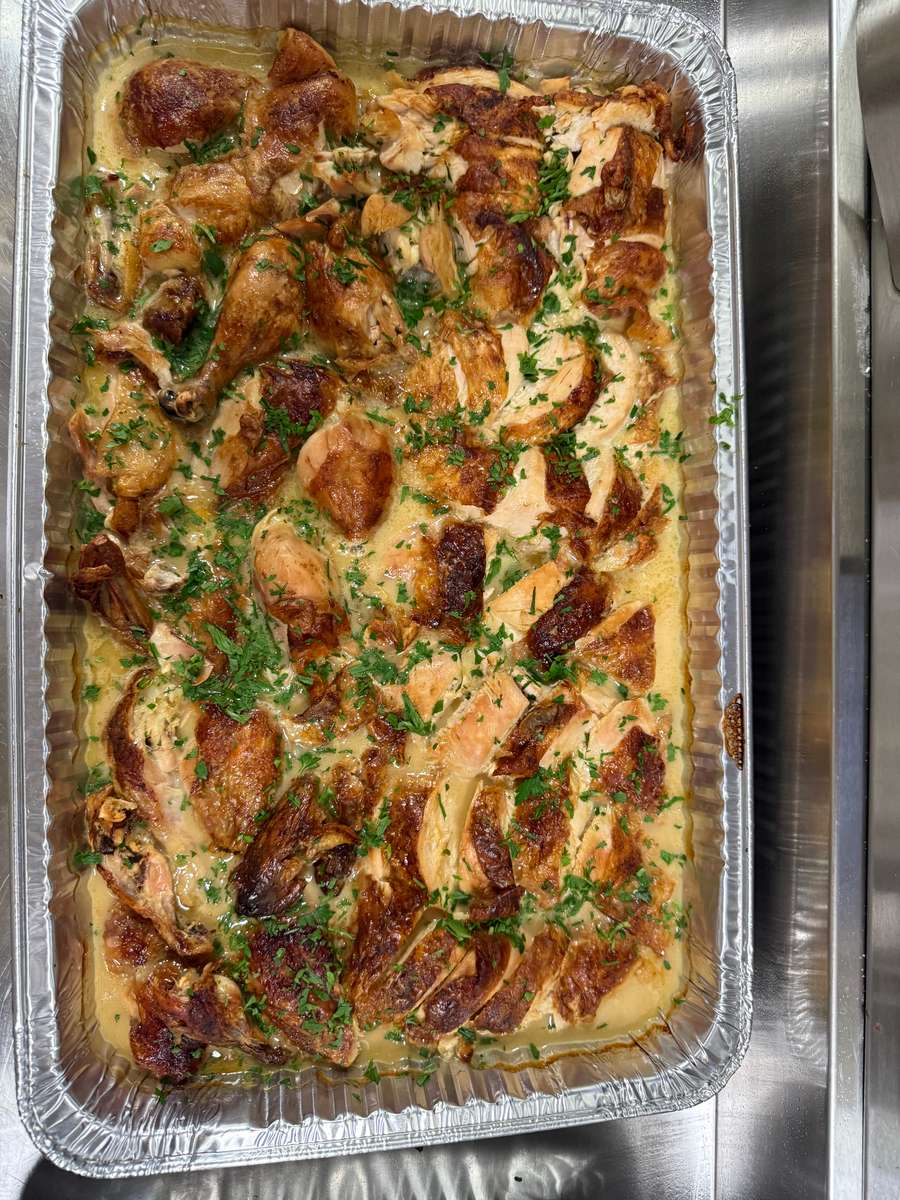 Tray of roasted chicken pieces served in a creamy herb sauce, garnished with freshly chopped parsley—perfect for catering menus and comfort food offerings.