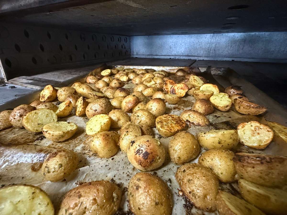 Golden herb-roasted baby potatoes cooking on a parchment-lined tray inside a commercial oven, seasoned to perfection for a crispy, flavorful side dish ideal for restaurant or catering menus.