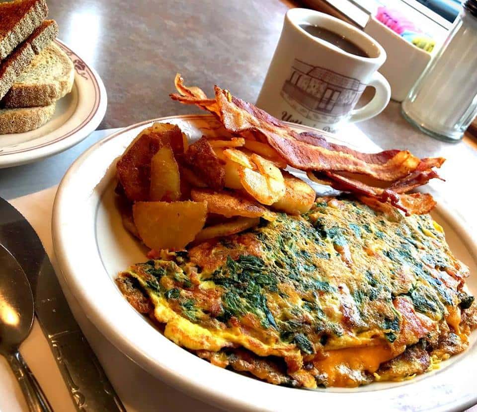 Omelette with spinach, tomato, and cheese with homefries, bacon, and a cup of coffee.