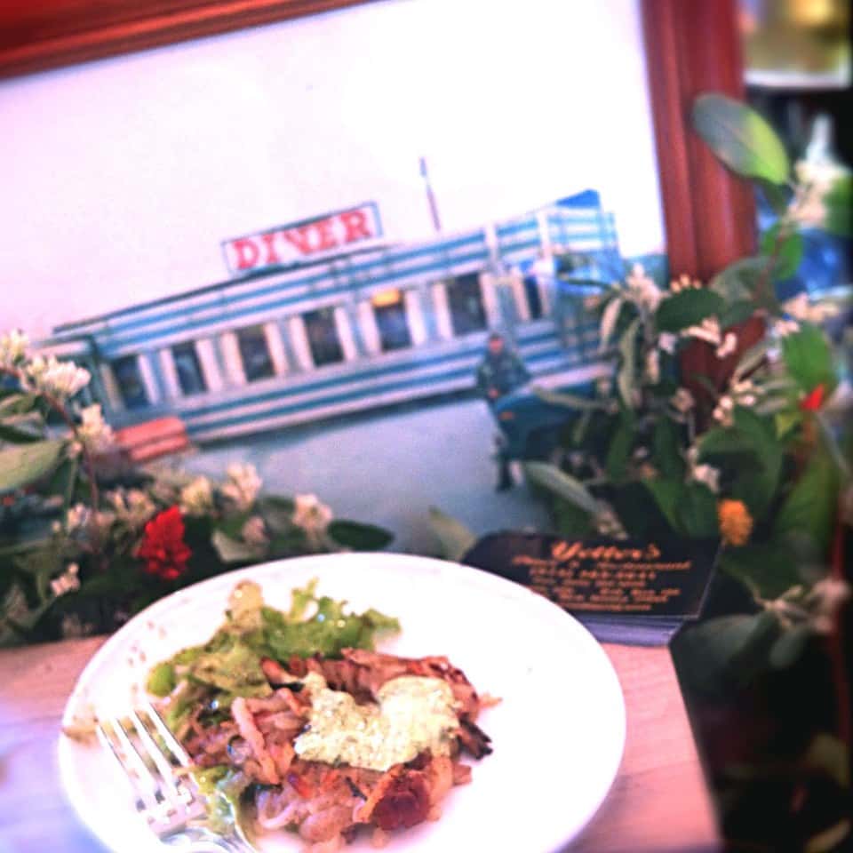 Chicken entree with salad on a white plate, picture of yetters diner in the background.