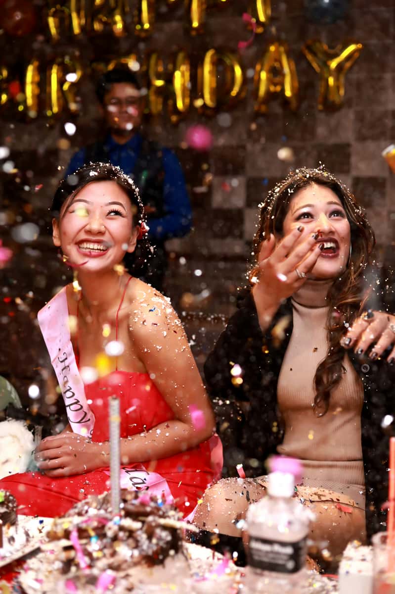 Two women celebrating at a birthday party with confetti, cake, and joyful expressions
