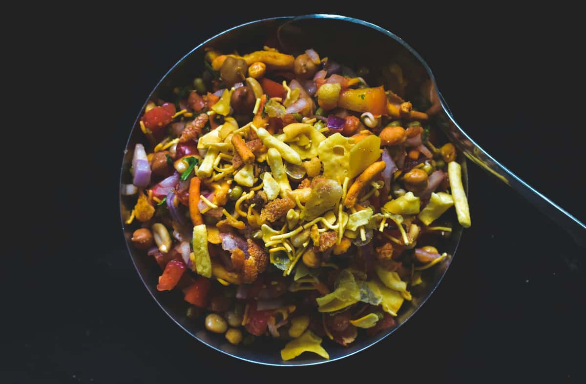 Top view of Indian bhel puri with sev, onions, tomatoes, and crunchy snacks in a metal bowl