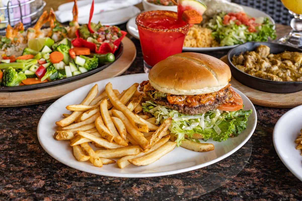 Juicy cheeseburger topped with lettuce, tomato, pickles, and crispy onions, served with French fries alongside colorful Tex-Mex favorites and handcrafted cocktails.