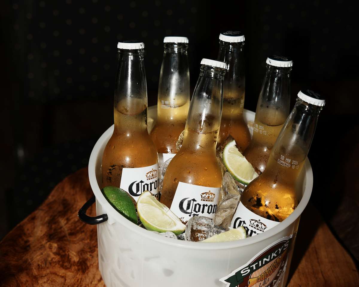 Bucket of Corona Extra beers on ice with lime wedges served in a branded Stinky's Fish Camp bucket.