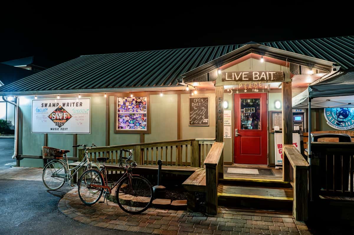 Stinky's Bait Shack entrance at night with a "Live Bait" sign, string lights, red door, and bicycles parked outside.