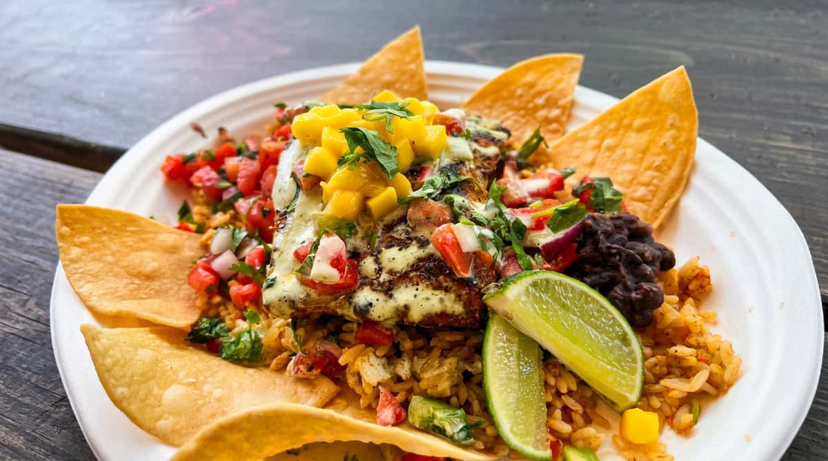 Grilled mahi-mahi over rice with mango salsa, pico de gallo, black beans, lime wedges, and chips.