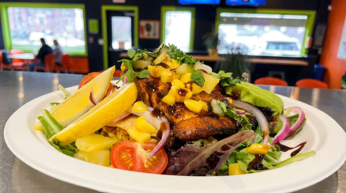 Grilled fish and mango salad with avocado, red onions, tomatoes, and lemon wedges on a white plate.